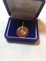 Front view of brown-orange agate donut pendant with gold bail and Chinese symbol accent inside blue jewelry box