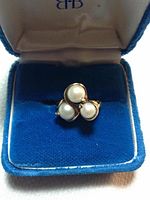 Ring displayed inside a blue and cream velvet jewelry box, showing three pearls set in a gold cluster design.