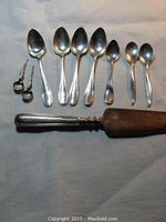 Nine assorted sterling silver spoons arranged in a row with two small ornate ones on the left and a cake knife with wooden blade and silver handle below.