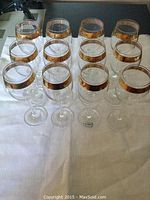 Set of twelve clear Bohemia crystal wine glasses with gold gilt rims, arranged on white cloth.
