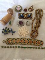 Overview photo showing all 12 pieces of antique costume jewellery including brooches, bracelets, necklaces, carved pendant, and perfume bottle.