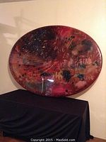 Photo showing entire oval-shaped painted fiberglass wall art placed on a table with black cloth under it, highlighting size and shape.