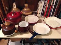Full display of 6 vintage enamel pot and pan pieces laid on shelf, highlighting overall condition and colors including maroon, brown, and blue with white interiors.