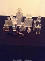 Front view of 12 assorted vintage and antique collectible perfume bottles arranged on black cloth background.