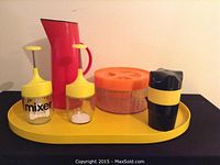 Photo showing all six items including red carafe, two yellow topped glass mixers, orange cookie container, black and yellow container, and yellow tray arranged together.
