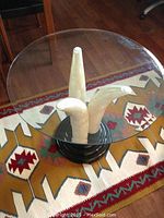 Overhead shot showing the round beveled glass top of the table and the arrangement of the three faux elephant tusks beneath it on a patterned rug.