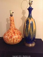 Two decorative ceramic lamps standing side by side, one with a bulbous orange-brown glaze and the other with a tall blue-yellow glaze and metal base.