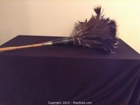 Antique ostrich feather duster laying horizontally showing feathers and wooden handle.