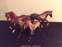 Group photo showing all four brown and tan Breyer horses arranged closely on a dark surface.