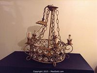 Full view of the antique chandelier showing the overall form, chain, and candle-style lights on a dark background.