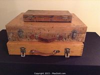 Three wooden artist paint boxes stacked, showing exterior with metal clasps and leather handles, paint-stained and worn.