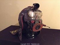Front angled view of artist made Mad Max style costume prop helmet showing mounted optics, protective goggles, mouth grill and leather neck guard.