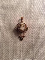 Front view of antique 9ct gold cameo pendant with seed pearls on textured fabric background