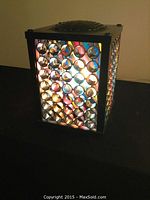 Front and side angle showing the cube-shaped lamp with circular reflective elements illuminated, showcasing colorful light effects.