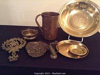 Overview of all brass items on black background including large pitcher, plaques, bowls, and trays.