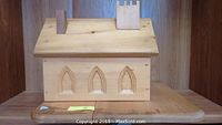 Front view of handmade wooden church model showing three arched window cutouts and roof detail with chimneys.