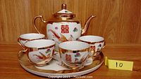 Full view of ceramic teapot, four cups, and oval tray with Chinese motifs and gold accents