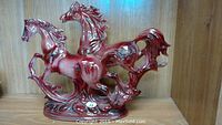 Porcelain figurine of two galloping horses in red and maroon shades on a base.