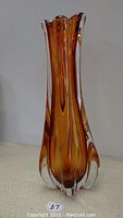 Full front view of amber glass vase showing fluted, elongated shape and scalloped top edge.