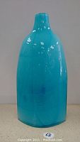 Photo of a tall, blue glass vase with a narrow neck and rounded edges on a neutral surface.