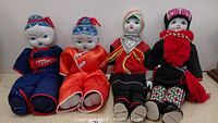 Four Chinese porcelain dolls sitting side by side, dressed in traditional colorful clothing with hand-painted porcelain heads.