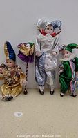 Four handcrafted porcelain dolls arranged side by side on a table, each wearing colorful and detailed costumes in jester and harlequin styles.