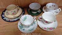 Photo shows five different tea cups paired with matching saucers arranged on a wooden shelf.