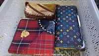 Photo of three wallets arranged in basket: red plaid, brown animal pattern, and black multicolor Louis Vuitton monogram wallet.