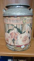 Front view of metal decorative jug showing two pigs and corn stalks with partial text reading 'WENT TO MARKET'