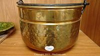 Brass bucket front view showing hammered texture and metal side handles.