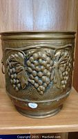 Front view of larger brass bucket showing detailed embossed grape cluster and leaves design