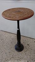 Full view of wood stand showing round top with carved floral design and turned pedestal base