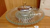 Photo of clear ridged glass serving tray with central glass bowl, metal domed lid and gold decorative handle on a wooden shelf.