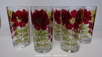 Six clear glass cups with red flower and green leaf designs arranged in a row.
