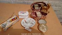 Photo showing all items on table including spoon with fruit decorations, floral trinket box, candle holder, rooster figurine on basket, and round metal trinket box.