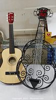 Photo shows a natural wood acoustic guitar next to a black ornamental iron guitar designed for wall decoration.