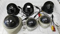 Overhead view of all six dome security cameras showing three black units with IR LED arrays and three beige dome units