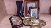 Group photo showing six assorted decorative picture frames on a wooden shelf, including floral, religious, and cherub art.