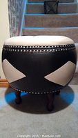 Front view of the round ottoman showing the white and black faux leather upholstery with silver nailhead trim.