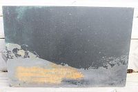 Full view of black slate or metal rectangular art piece with faded orange block printed text, showing distressed edges and surface.