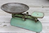 Side angle of antique green metal balance scale showing bowl and platform