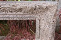 Close-up showing the textured paint with carved details on the wood frame, resembling a stone finish with visible wear.