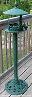 Full view of green cast iron bird feeder on a deck, showing height and structure.