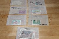 Photo of seven envelopes each containing sets of vintage stamps from various countries, with visible labels indicating country and set info.