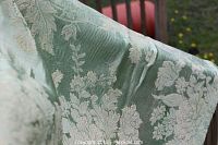 Close up of folded green silk-satin brocade fabric showing raised floral and leaf pattern and fabric texture.
