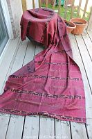 Full view of the reddish-purple silk sarong laid over a stool and flowing down to the wooden deck floor showing length and color