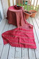 Full length draped view of antique red and gold patola ikat sarong/shawl on outdoor wooden deck with potted plants in background.