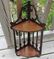 Photograph of antique Victorian-style carved walnut corner wall bracket with two wooden triangular shelves and ornate openwork design, displayed outdoors on wooden railing.