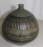 Full front view of round bottle-form vase showing overall shape and incised linear pattern under grey-green glaze