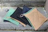 Set of eight square hemp pot holders/hot pads in various colors arranged on a stone surface, showing their quilted diamond pattern and hanging loops.